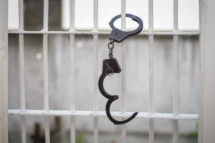 680970664 Handcuffs hanging on white metal bars.
