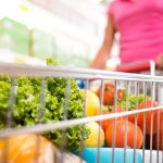 A shopping cart filled with fresh vegetables and fruits in a supermarket