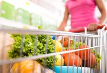 A shopping cart filled with fresh vegetables and fruits in a supermarket