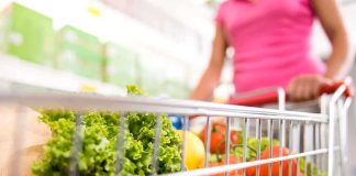A shopping cart filled with fresh vegetables and fruits in a supermarket