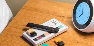 Vape pen, smartphone, clock on wooden table.