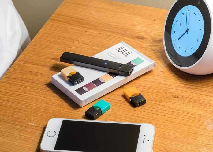 Vape pen, smartphone, clock on wooden table.