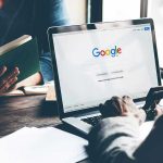 Laptop on Google homepage, person reading a book.