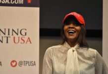 A woman wearing a red cap and a white blouse speaking at a political event