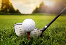 A golf ball on a tee with a golf club resting beside it on green grass