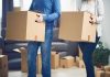 Two people carrying cardboard boxes indoors.
