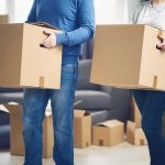 MASS Exodus: Thousands FLEEING State! Two people carrying cardboard boxes indoors.