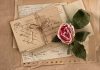 Centuries Old Letter DISCOVERED—What Did It Reveal? A collection of vintage postcards and a dried rose arranged on a textured background