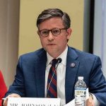 A public official speaking at a meeting with a nameplate in front of him