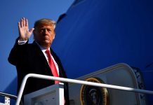 A political figure waving while standing on the steps of an aircraft