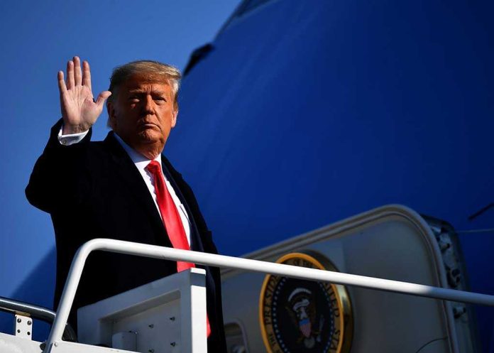 A political figure waving while standing on the steps of an aircraft