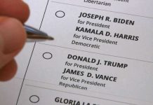 Hand holding pen near presidential election ballot.