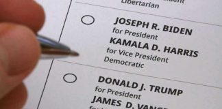 Hand holding pen near presidential election ballot.