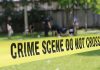 Police Officer’s Shocking Murder-Suicide Unveiled Yellow crime scene tape blocking grassy area.