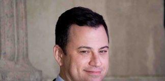 A smiling man in a suit with a confident expression against a neutral background
