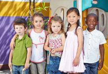 Five children standing together in a playground setting, smiling at the camera