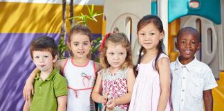 Five children standing together in a playground setting, smiling at the camera