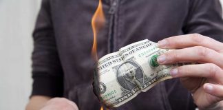 A person holding a burning dollar bill with a match in the other hand
