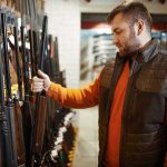 Man examining rifles in a store.