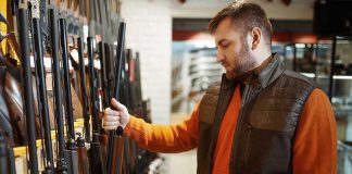Man examining rifles in a store.