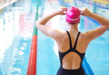 A female swimmer adjusting her pink swim cap at the edge of an indoor swimming pool