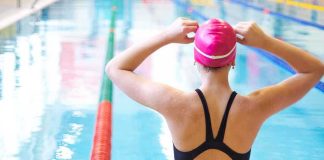 A female swimmer adjusting her pink swim cap at the edge of an indoor swimming pool