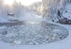 A serene winter landscape featuring a frozen lake surrounded by snow-covered trees and a log cabin