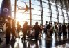 Crowd of travelers in airport terminal with airplane outside.