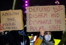 Two individuals holding protest signs with messages about police reform