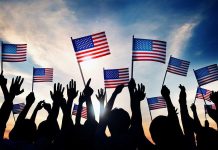 Silhouetted crowd holding American flags against a sunset sky