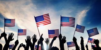 Silhouetted crowd holding American flags against a sunset sky