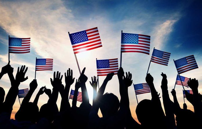 Silhouetted crowd holding American flags against a sunset sky