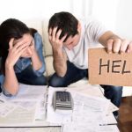 A distressed couple surrounded by paperwork, with one holding a sign that says HELP