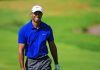 Back Surgery Number 7: Can Tiger Woods Return? A smiling golfer wearing a blue shirt and white cap on a green golf course