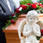 Statue of angel in front of coffin with roses.