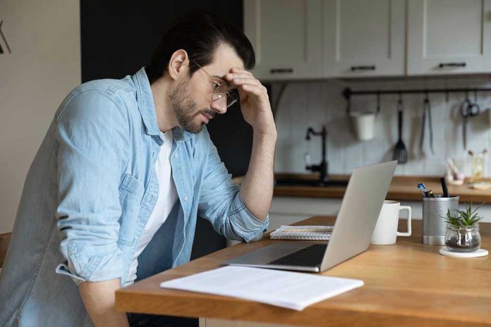 Man stressing over work on laptop at kitchen table.