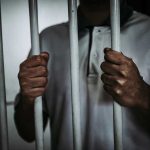 Person holding jail cell bars tightly.