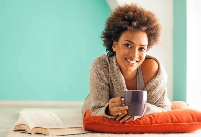 A woman lying on a cushion with a coffee cup, smiling at the camera