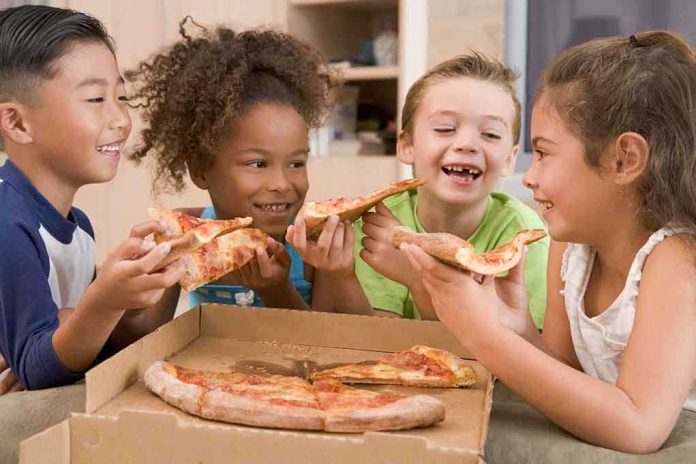 Four children joyfully sharing slices of pizza around a box