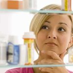 Menstrual Leave Fight Explodes—Hiring Panic Next? A woman thoughtfully looking at a medicine cabinet filled with various medications