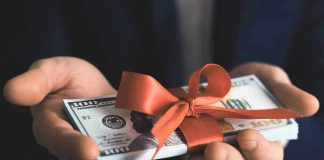 Fake Charity Funneled Cash To Hamas? Hands holding stack of hundred-dollar bills with ribbon.