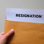 A hand holding an envelope with a resignation letter partially visible