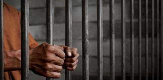 Governor Draws Hard Line On Inmate Care Hands gripping prison cell bars.