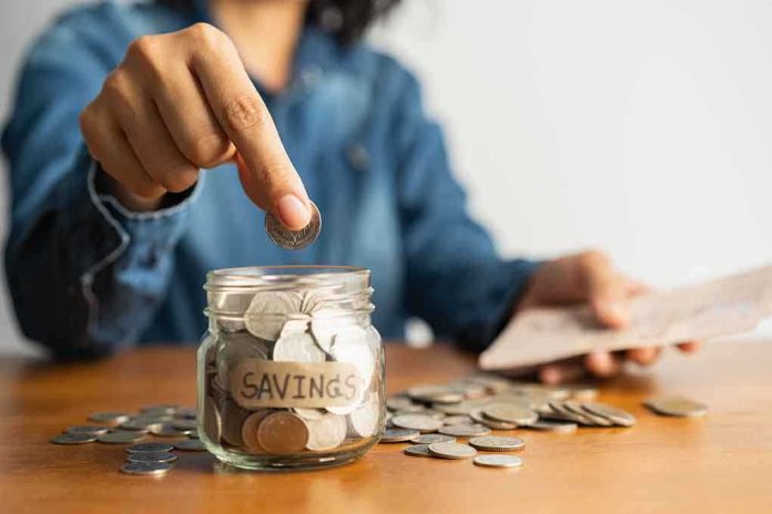 shutterstock_1523822675 Person placing a coin into a savings jar labeled 'SAVINGS'