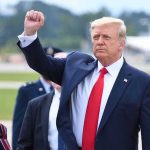 Somber Flight Home: Trump Salutes Fallen man in suit raising a clenched fist outdoors