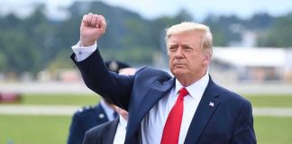 Somber Flight Home: Trump Salutes Fallen man in suit raising a clenched fist outdoors
