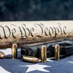Gun, bullets, Constitution scroll on American flag.