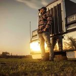 Truck driver standing beside a semi truck at sunset