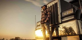Truck driver standing beside a semi truck at sunset