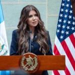 A government official delivering a speech at a podium with flags in the background